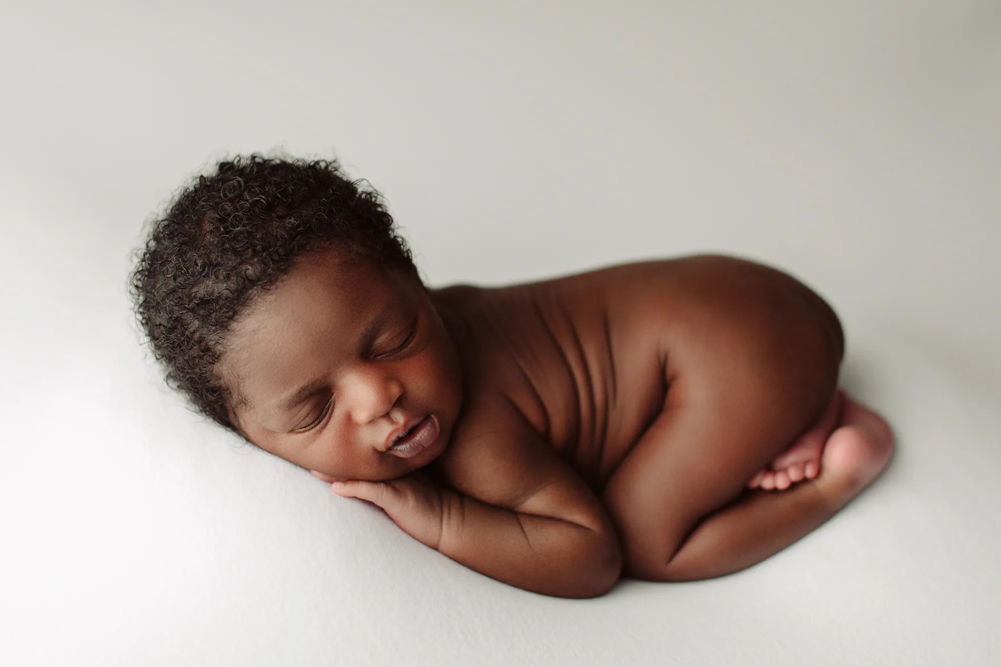 Newborn curled up asleep on a white backdrop