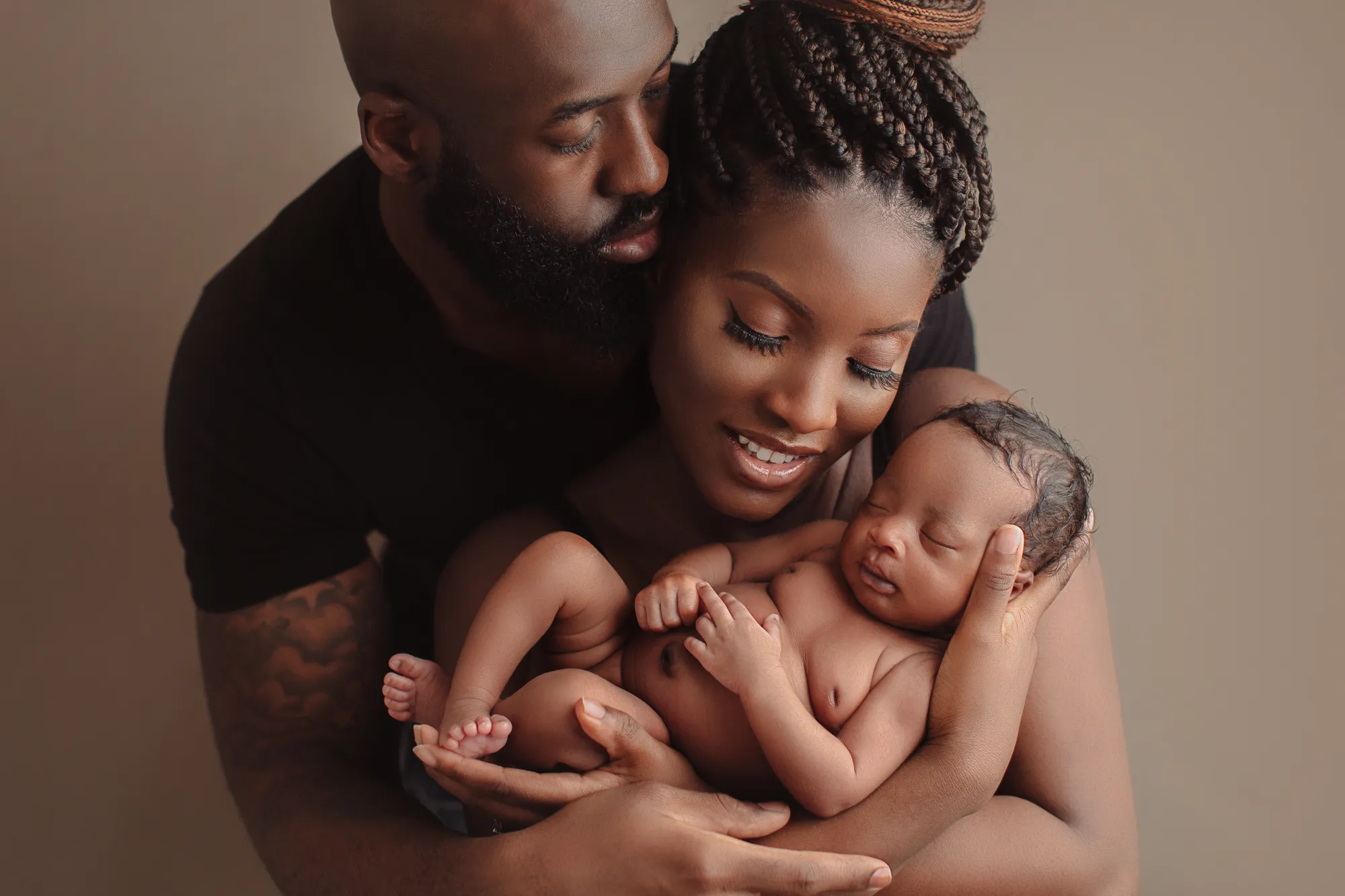 Parents embracing their newborn baby against a taupe backdrop