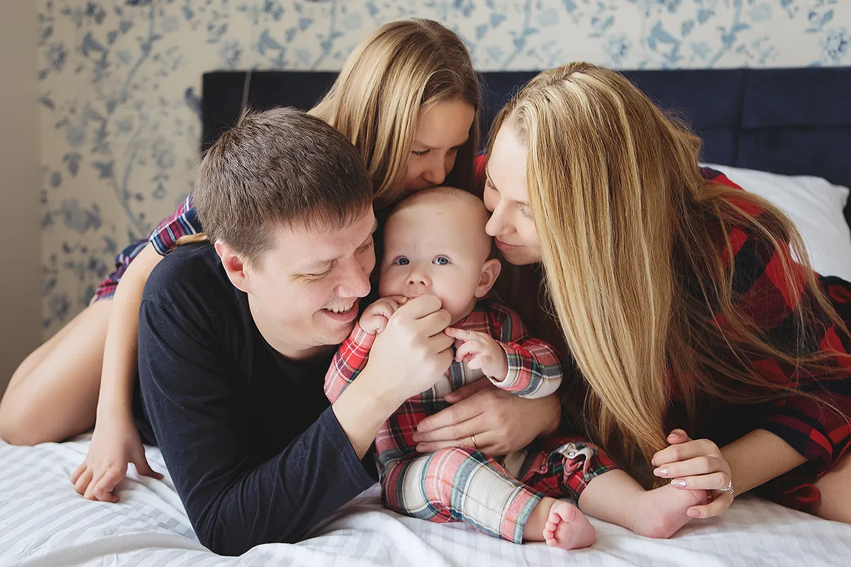 Parents and big sister kissing a baby on a bed