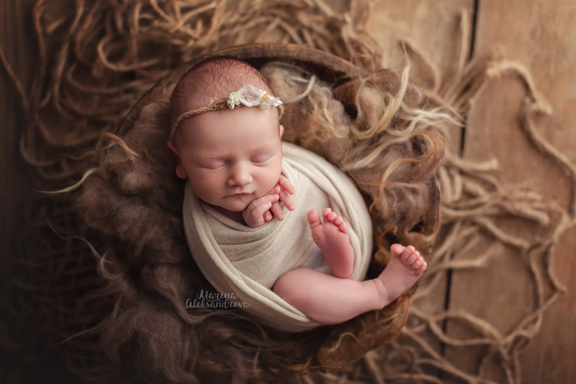 Newborn swaddled in cream asleep in a nest of jute and fur
