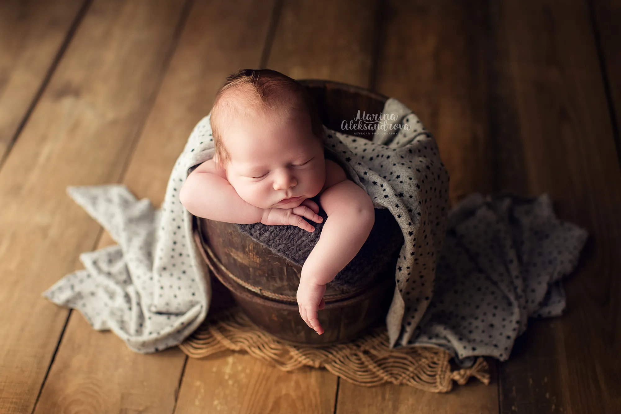 Newborn resting in a wooden bucket under a polka-dot blanket