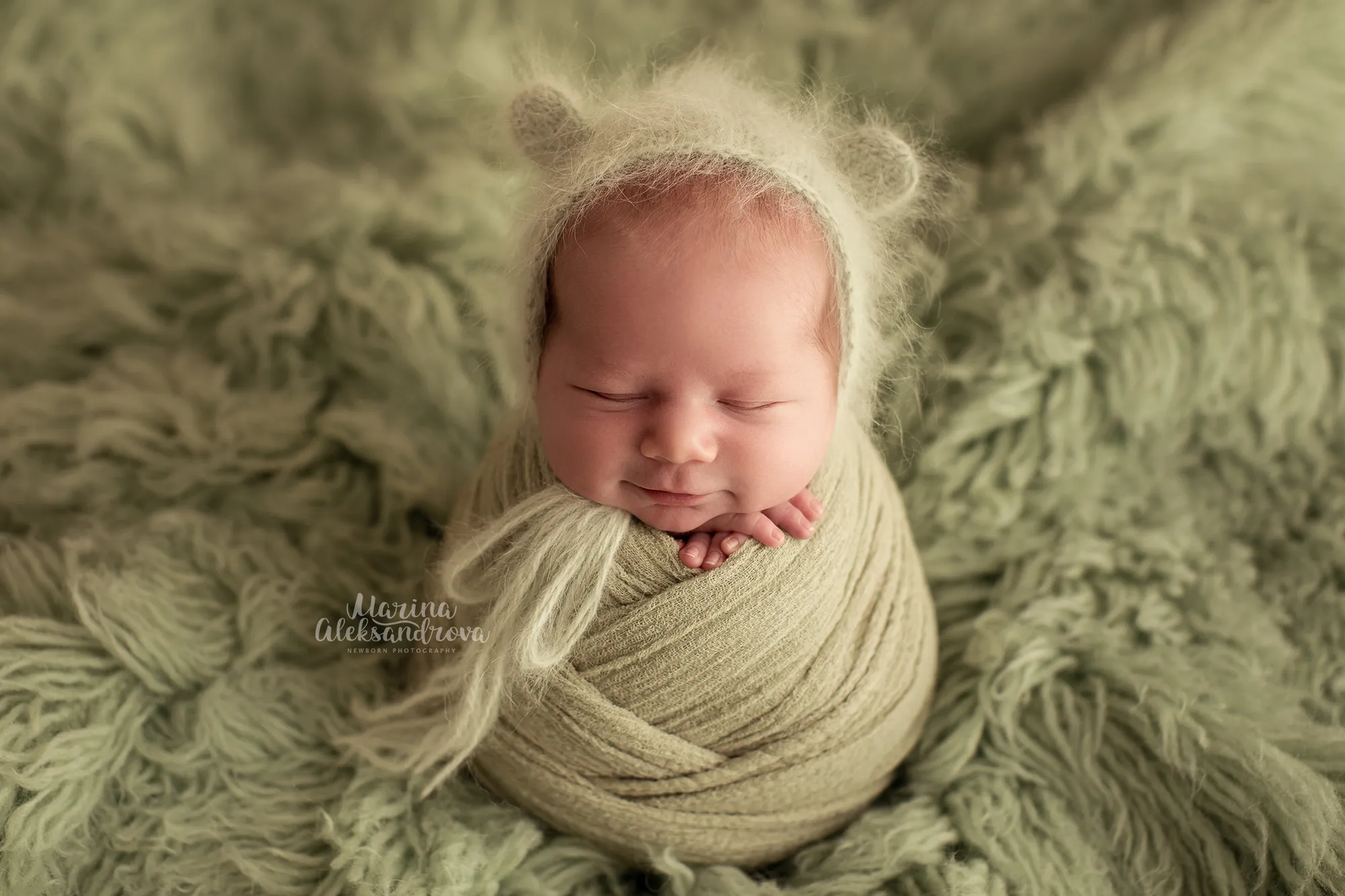 Newborn in a teddy-ear bonnet swaddled in olive green on olive fur