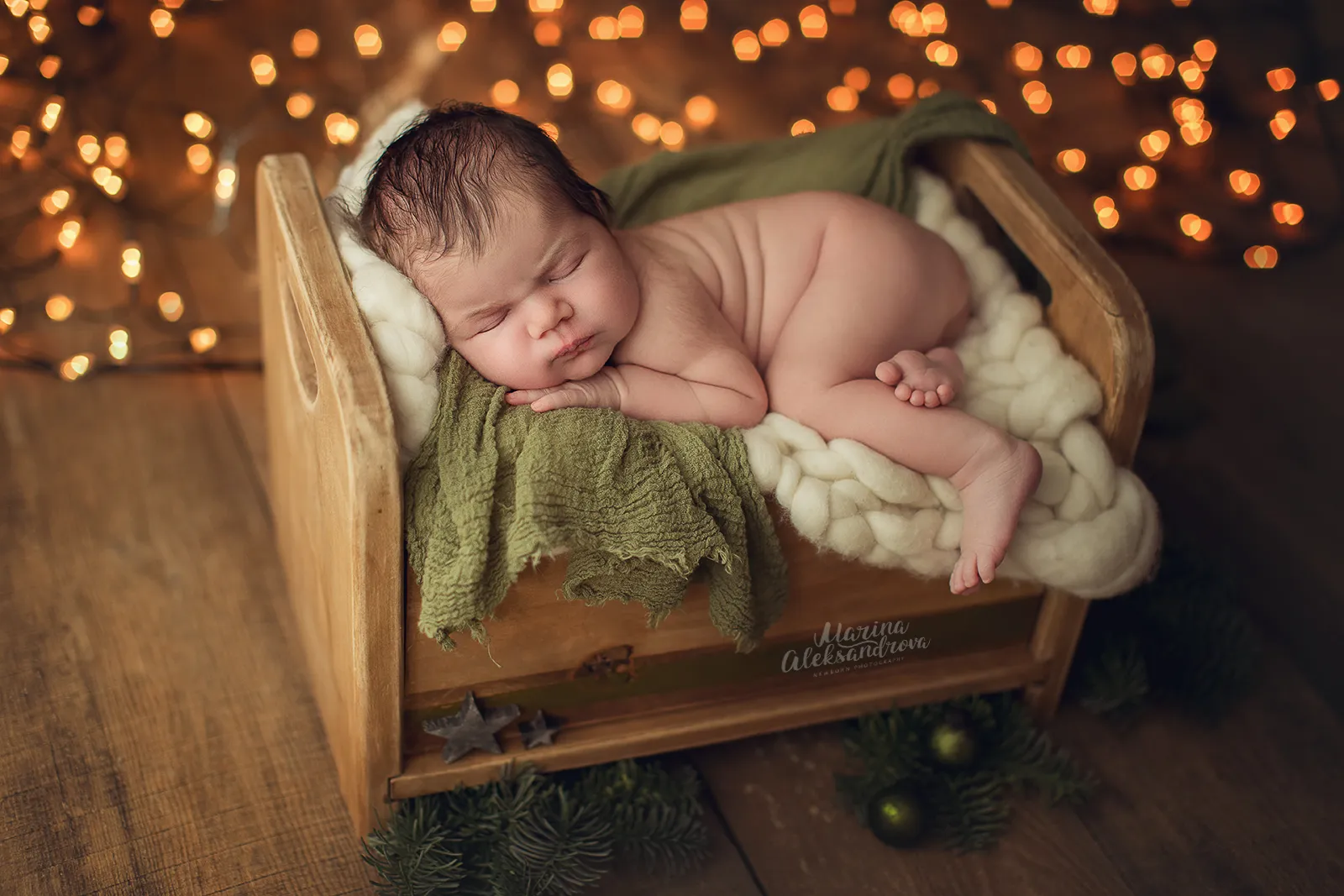 Newborn asleep on a cream blanket in a wooden bed with fairy lights behind