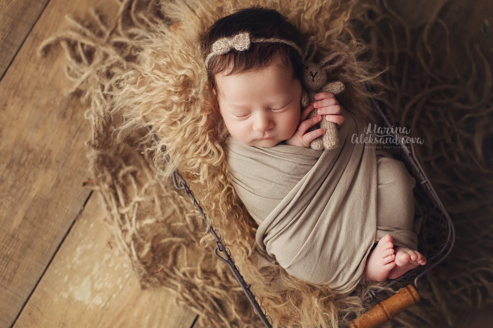 Newborn swaddled in taupe with a bow headband in a basket on jute